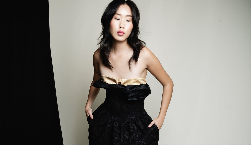 Woman wearing a black dress with a gold top against a plain background